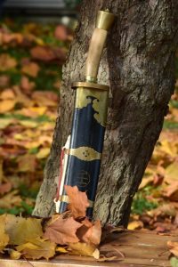 Broadsword in scabbard leaning on a tree surrounded by autumn leaves